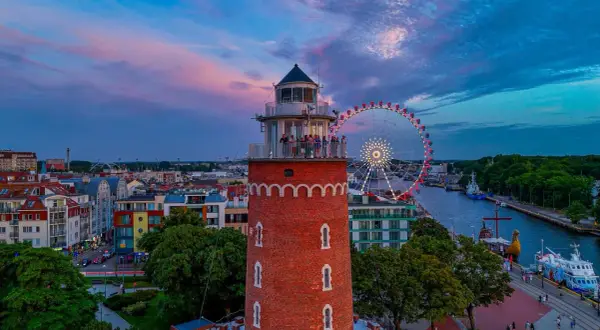 Widok na latarnię morską, diabelski młyn i port w Kołobrzegu o zachodzie słońca.